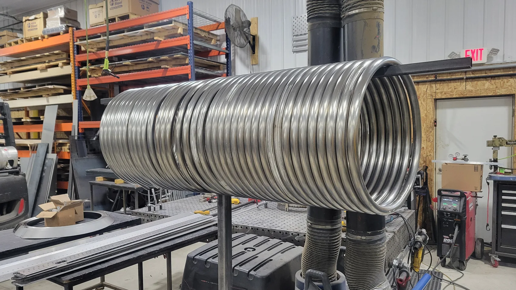 Long precision-rolled helical stainless steel coil mounted on a welding stand in the Sons of Thunder shop