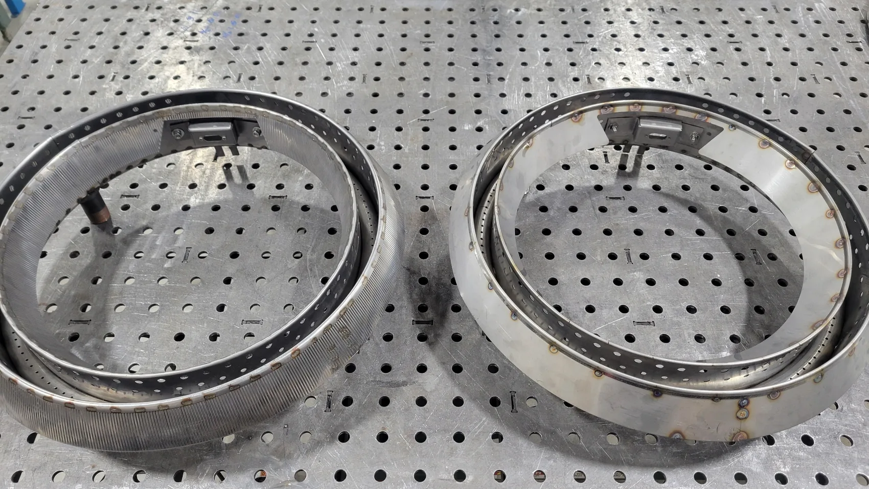 Two finished TIG-welded perforated stainless burner cans, side by side and dialed to the same spec.