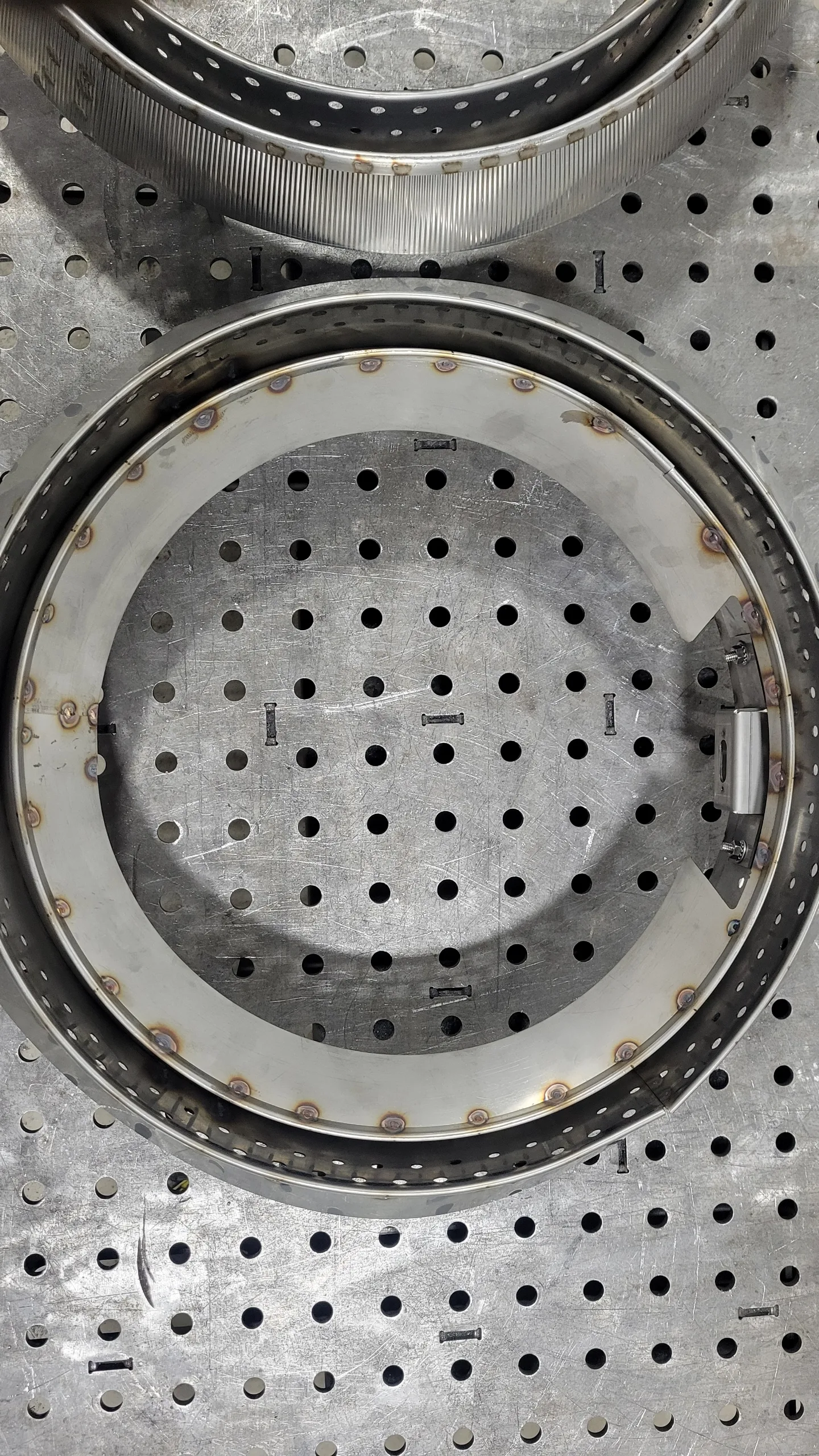 Detail of a finished burner can: the threaded NPT nipple welded into the perforated stainless body, TIG seam clean and consistent.