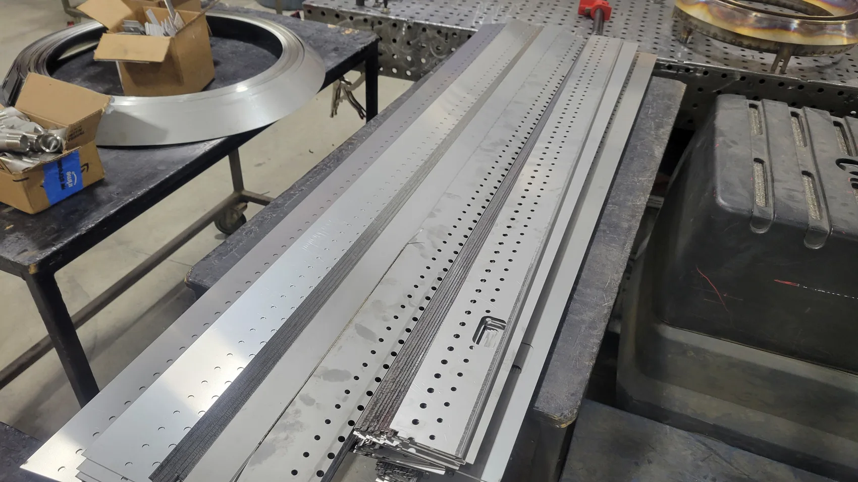 Laser-perforated stainless strips laid out in batch, every hole pattern identical down the run.