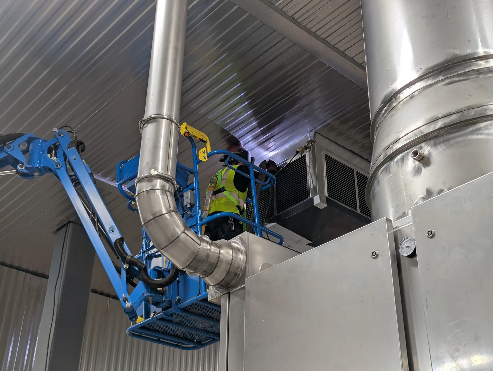 Welder on a boom lift TIG-welding stainless duct overhead in a cold-storage plant