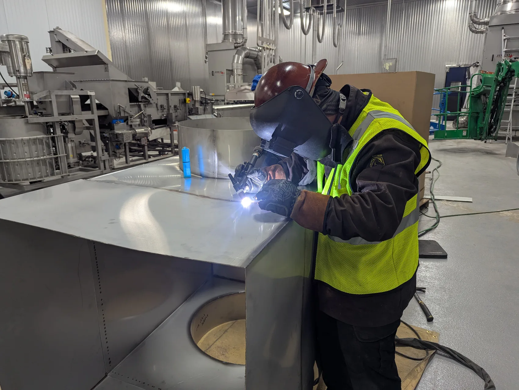 TIG-welding the 66-inch square stainless exhaust duct in place on site - food-grade GTAW on heavy-gauge stainless.
