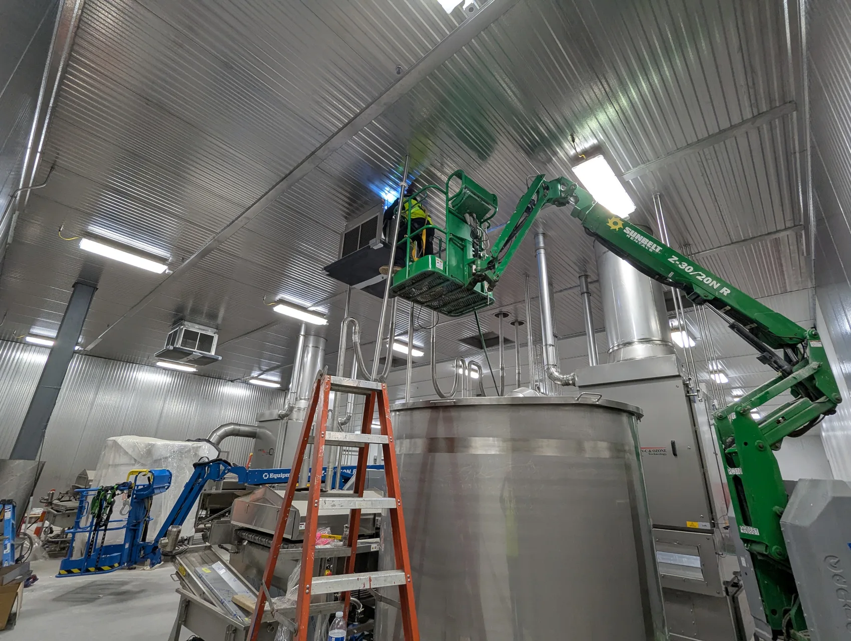 Boom-lift field install: tying the overhead spiral stainless duct into the unit, working in the active plant.