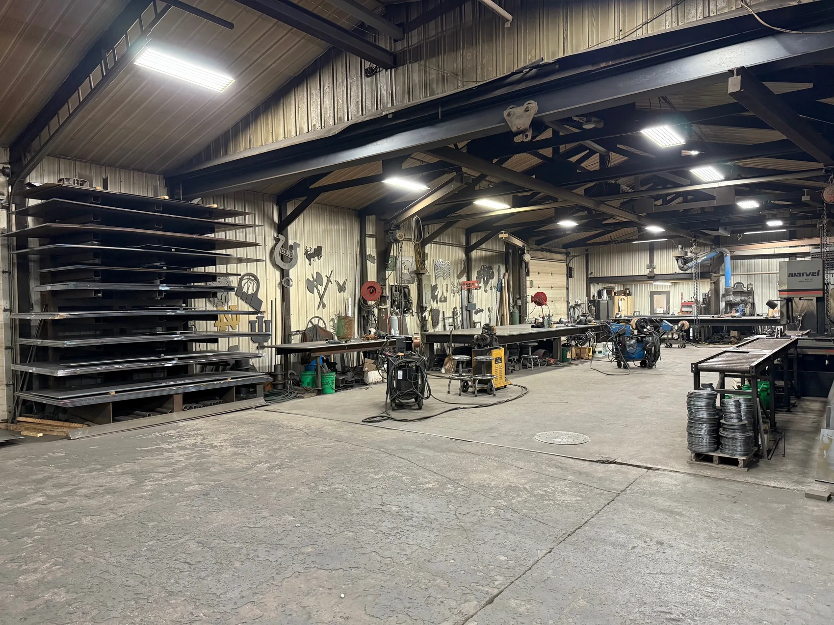 Open fabrication shop bay with steel plate racks, band saw, welding stations and drill press