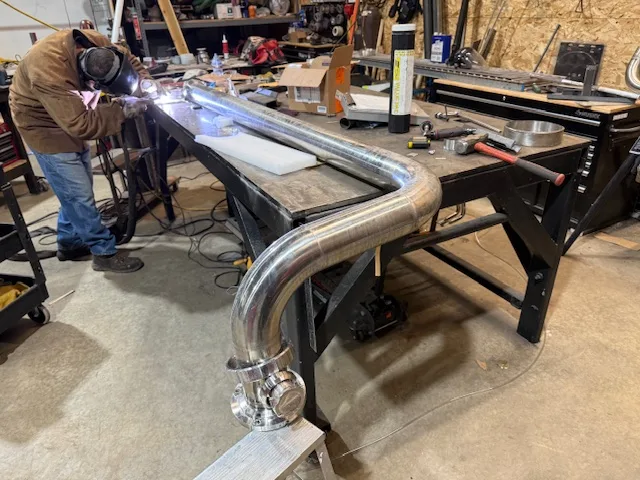 Welder TIG-welding polished stainless tube assemblies on a shop bench by Sons of Thunder Welding