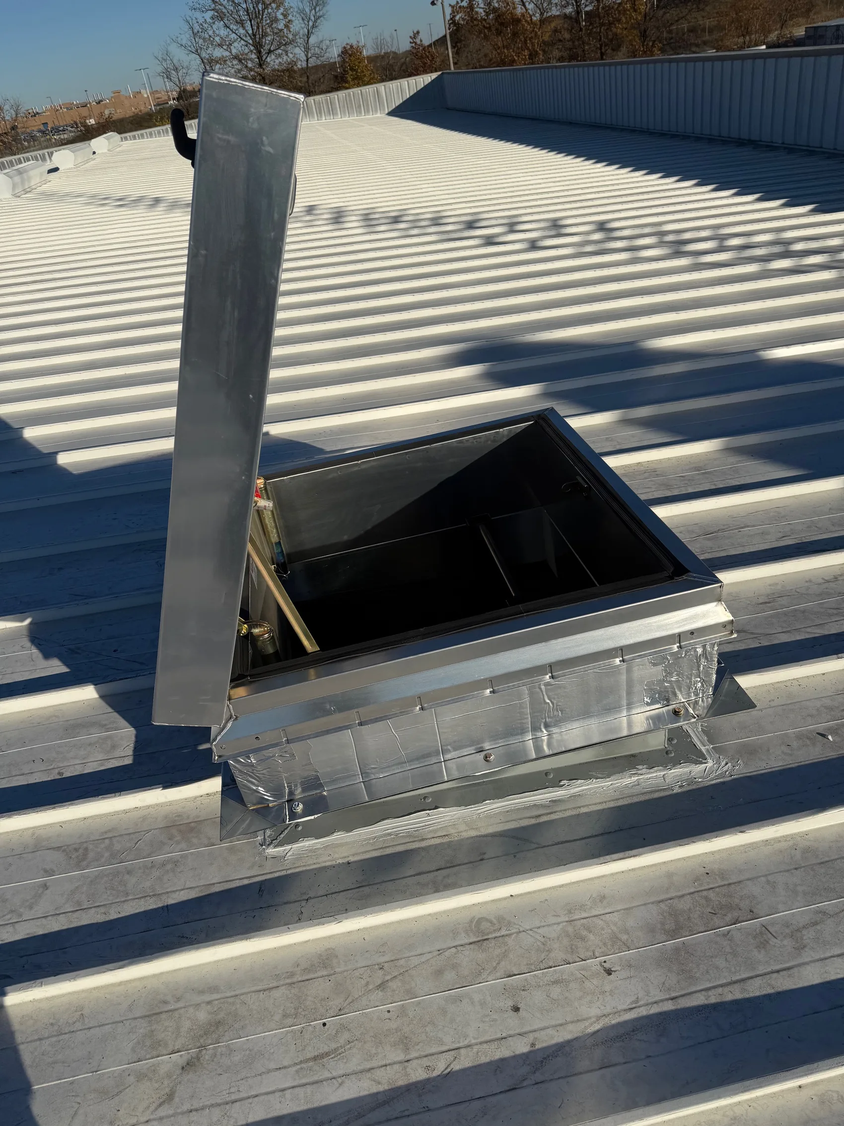 The finished roof access hatch open on the standing-seam metal roof, flashed and sealed into the panel run.