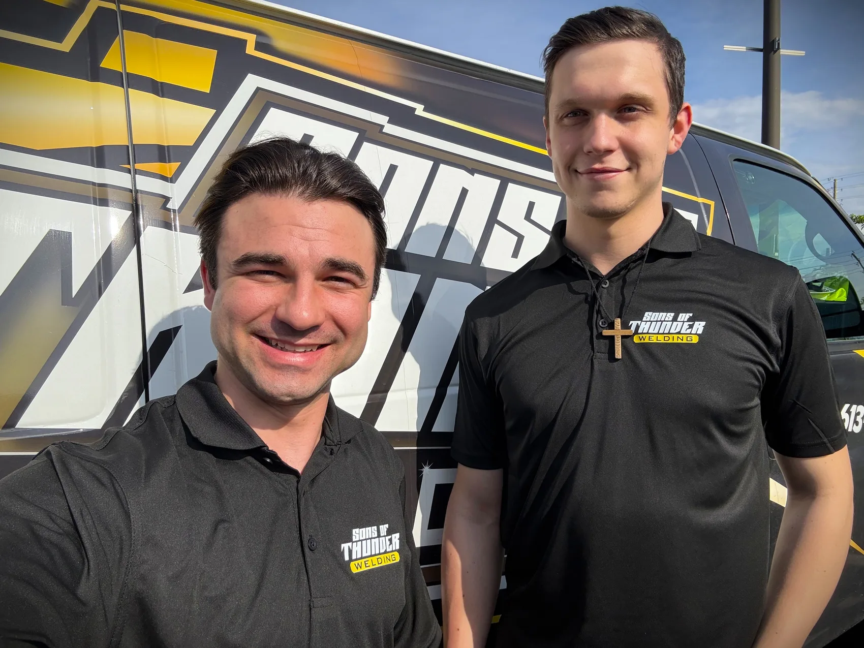 Two Sons of Thunder team members in branded polo shirts in front of the company van