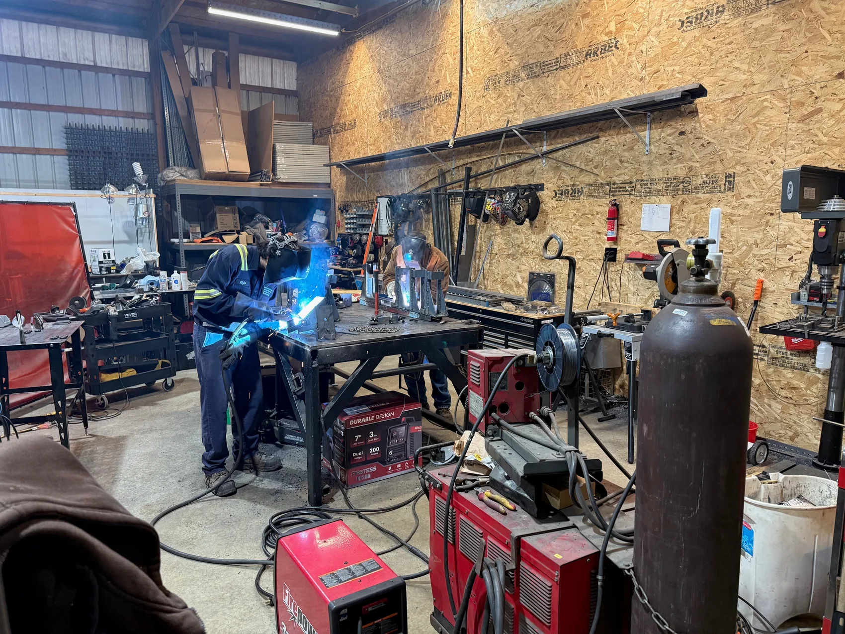 Two welders working together with a blue TIG arc in the Sons of Thunder shop